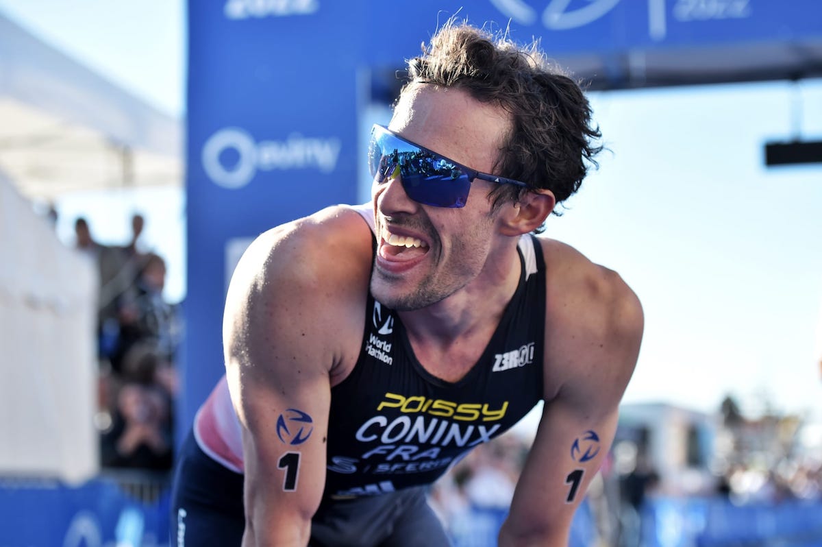 dorian_coninx_bergen_world_triathlon_2022 French triathlete Dorian Coninx wearing sunglasses and smiling to someone off camera puts his hands on his knees as he catches his breath after winning the 2022 Bergen World Cup