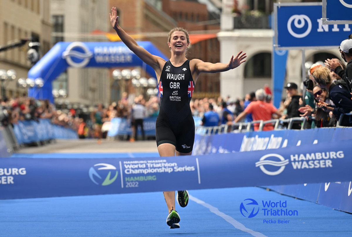 2022 World Triathlon Championship Series Hamburg | Mixed Relay GB triathlete Kate Waugh running towards the finish line with arms aloft to give Team GB the mixed team Relay world title, in Hamburg 2022.