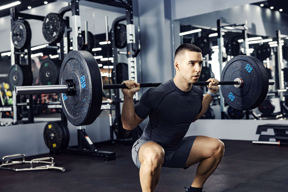 A young male doing deadlift and exercising with barbell in a gym