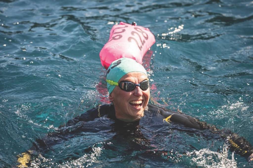 Woman wearing swim cap, goggles and wetsuit smiles in the water