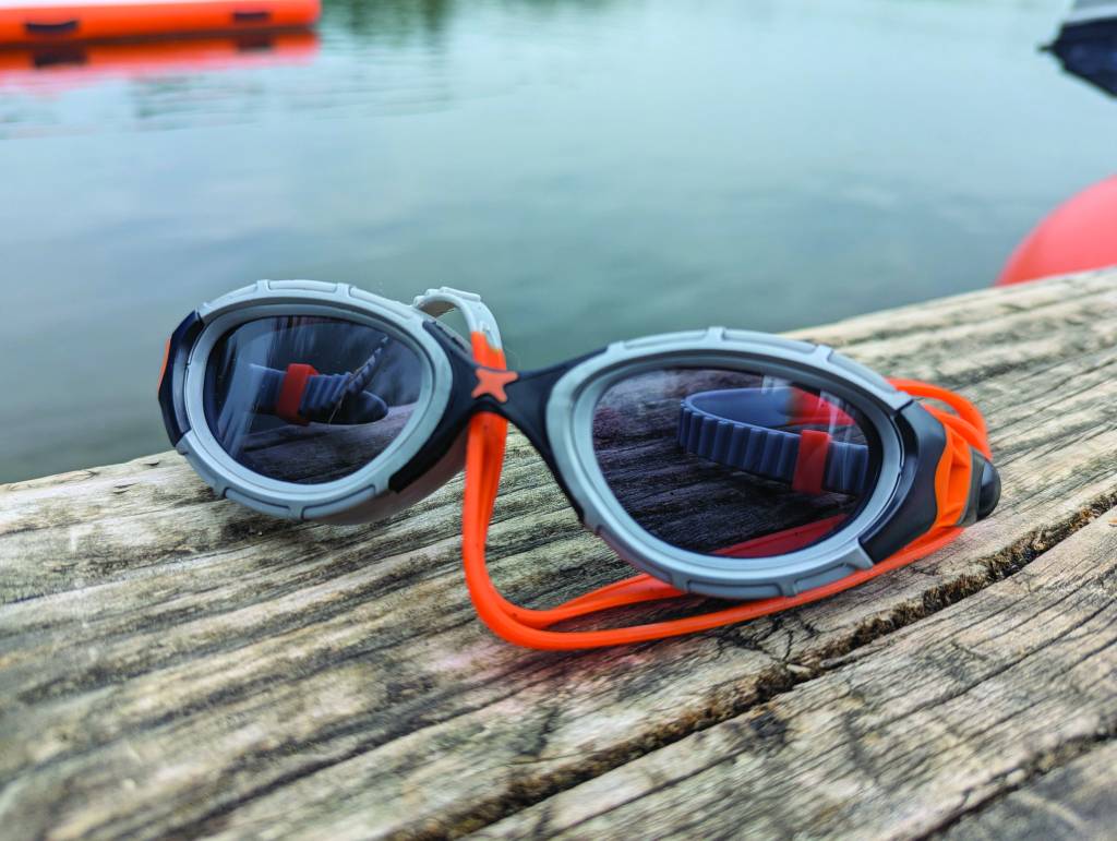 Black and orange Zoggs Predator flex swim goggles resting on wood by water
