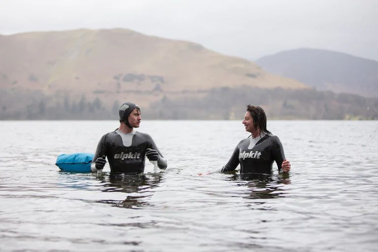 Man and woman in open water wearing black and silver wetsuits