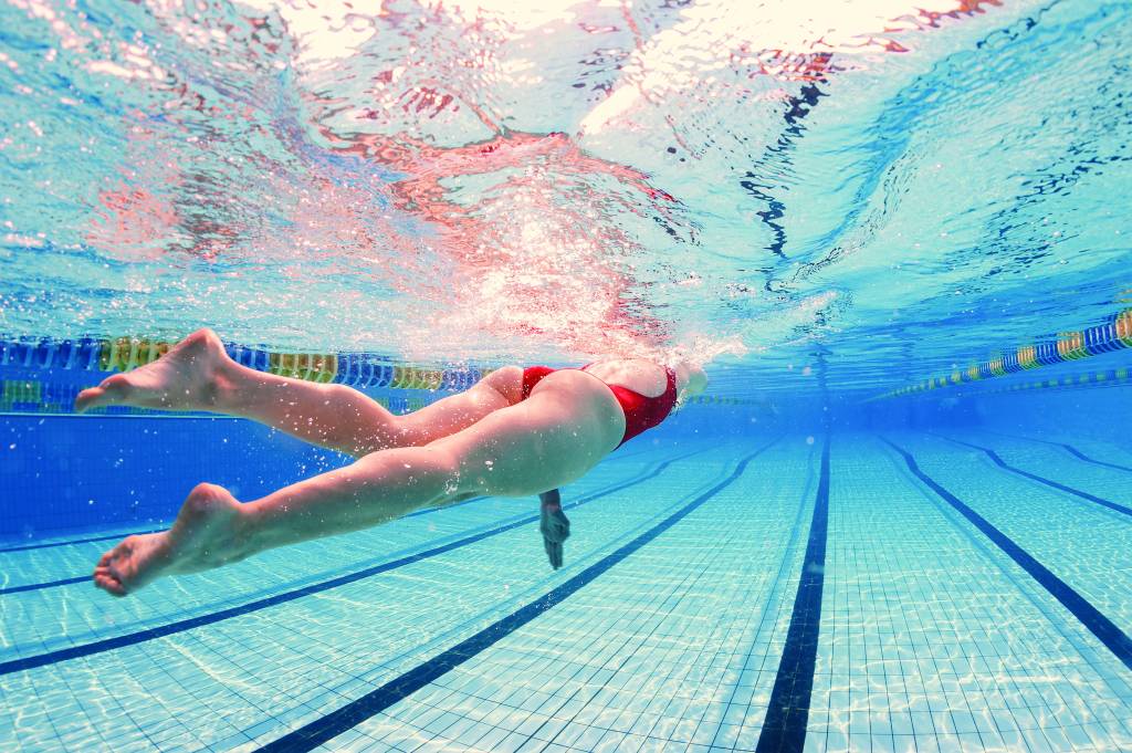 Woman professional swimmer wearing red swimsuit inside swimming pool.