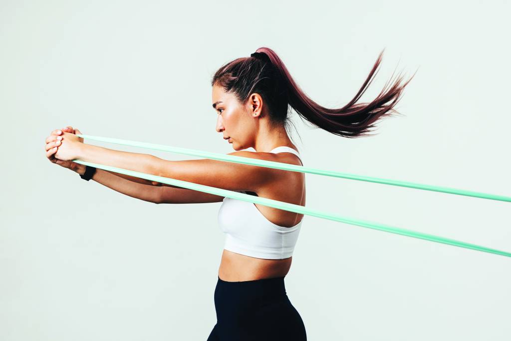 Side view of sportswoman exercising with resistance band against white wall
