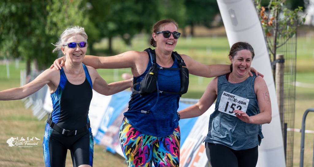 Three women celebrating crossing the finish line of their triathlon, arms linked with one another 