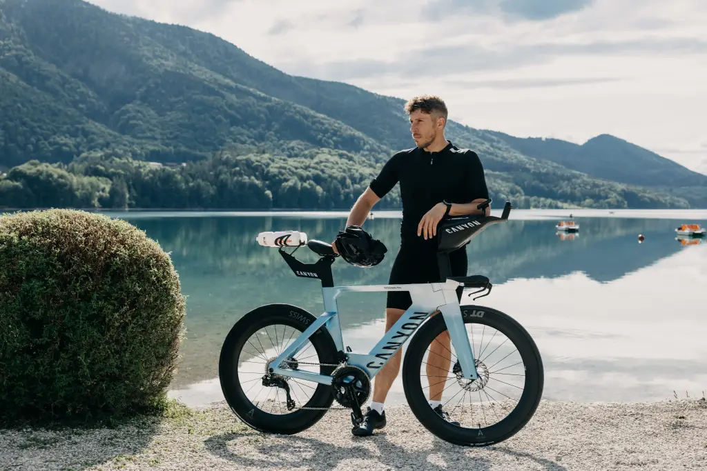 Man standing by a tri bike next to a lake